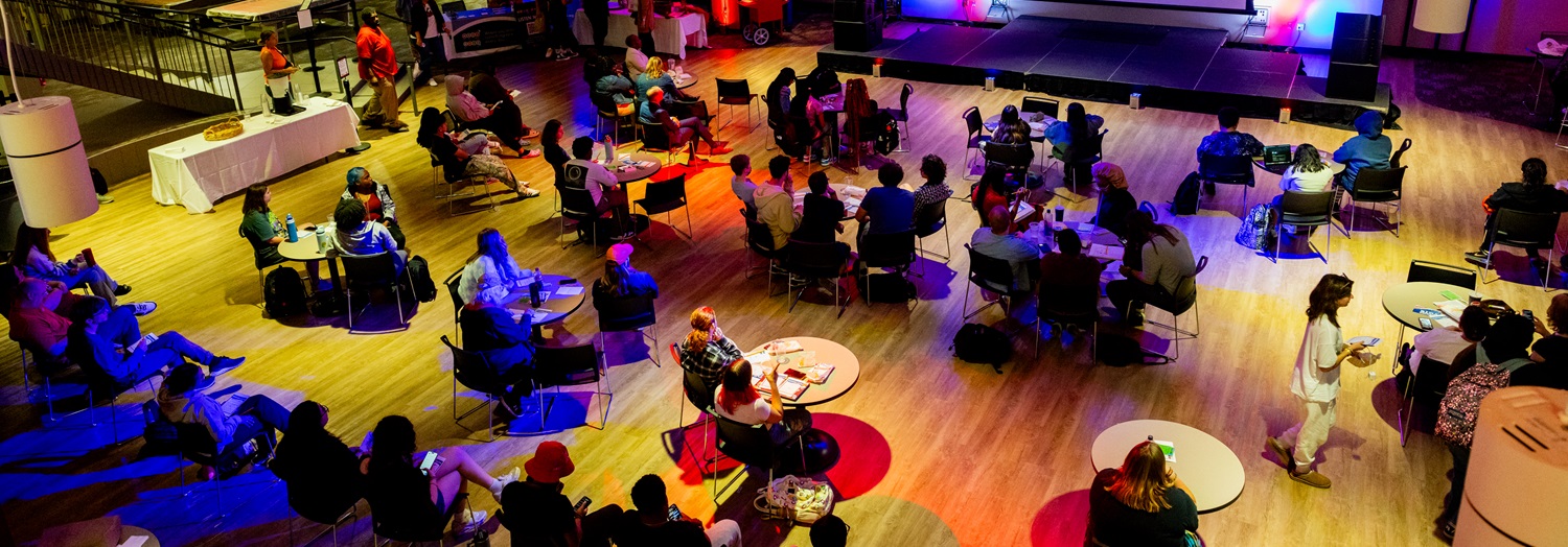 A large group of attendees sitting at round tables in the HSC Huskie Den for an event